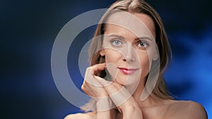 Closeup face of young smiling woman posing stroking chin isolated at blurred neon bokeh