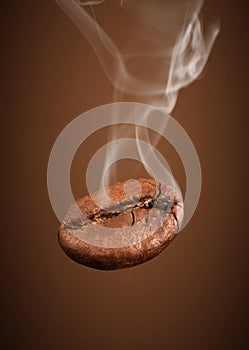 Closeup falling coffee bean with smoke on brown background