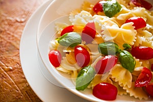 Closeup of Farfalle pasta with cherry tomatoes and basil over a colored background