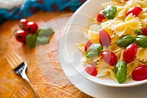 Closeup of Farfalle pasta with cherry tomatoes and basil over a colored background and fork