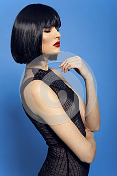 Closeup fashion portrait of a young beautiful dark-haired woman with red lip, over blue background.