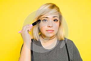 Closeup of a fat woman with dyed hair putting on some makeup with a brush and making eye contact