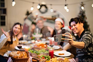 Closeup father hand holding mobile phone for capture selfie Asian family group celebrating in Happy Christmas Eve dinner feast