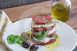 Closeup Caprese Salad with sliced red tomato, buffalo mozzarella, basil leaves and healthy whole olives dripping in extra virgin o