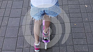 Closeup of the feet of a child riding a scooter in the summer.