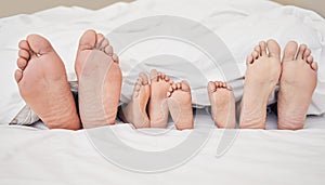 Closeup of feet of family lying in bed. Bare feet of parents and children sticking out in bed. Family with two children