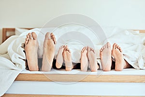 Closeup of feet of family lying in bed. Bare feet of parents and children sticking out in bed. Family with two children