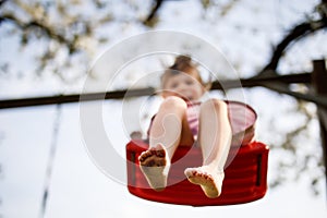 Closeup of feet of little toddler girl having fun on swing in domestic garden. Small child swinging under blooming trees