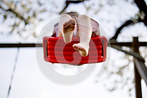 Closeup of feet of little toddler girl having fun on swing in domestic garden. Small child swinging under blooming trees