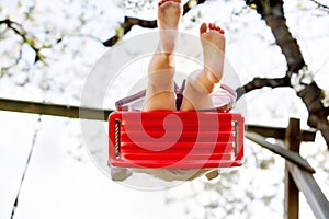 Closeup of feet of little toddler girl having fun on swing in domestic garden. Small child swinging under blooming trees