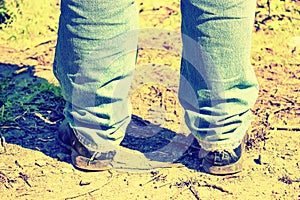 Closeup of feet of a man in old blue jeans and old shoes. Tinted.