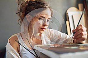 Closeup of a female artist painting on canvas in her art studio. A woman painter with transparent eyeglasses painting with oil in