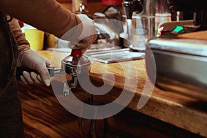 Closeup of female barista`s hands tempering, pressing ground coffee in metal portafilter. Tamping coffee