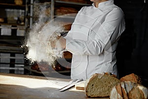 Closeup female chef hands clapping in cloud of powdery flour over table