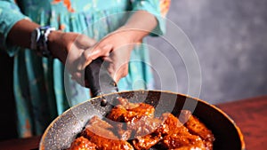 Closeup of a female chef tossing crispy fried hot buffalo chicken wings in a pan