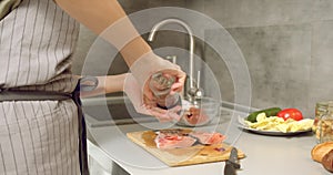 Closeup female cook hands cooking and sprinkling ground black pepper slices of salmon filet in the kitchen