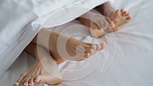 Closeup of female couple play and dance their feet under blanket while wake up in bed in morning