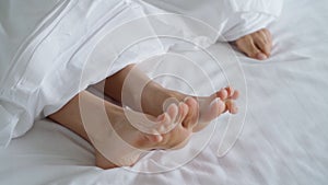 Closeup of female couple play and dance their feet under blanket while wake up in bed in morning