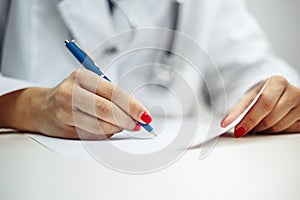 Closeup of a female doctor hands with a blue pen making notes and filling in diagnosis of patient on a paper. Coronavirus test and photo