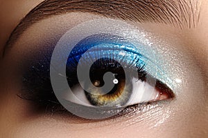 Closeup female eye with beautiful fashion bright make-up. Beautiful shiny blue eyeshadow, wet glitter, black eyeliner