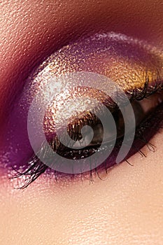 Closeup female eye with beautiful fashion bright make-up. Beautiful shiny gold, purple eyeshadow, wet glitter