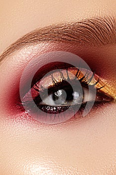 Closeup female eye with fashion bright make-up. Beautiful gold, red eyeshadow, glitter, black eyeliner. Shape Eyebrows