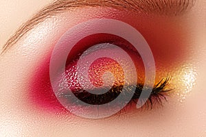 Closeup female eye with fashion bright make-up. Beautiful shiny gold, pink eyeshadow, wet glitter, black eyeliner