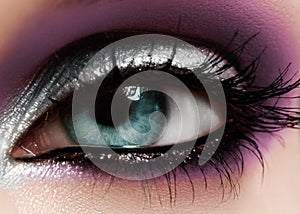 Closeup female eye with fashion bright make-up. Beautiful shiny silver, purple eyeshadow, wet glitter, black eyeliner