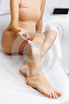 Closeup of female feet with smooth skin and soft feather on white background. Young Woman& x27;s Hand Touhing Her Legs photo