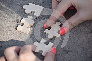 Closeup of female fingers with manicure putting wooden blank puzzle pieces together