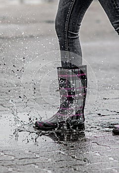 Closeup of a female foot in a stylish rubber boot jumping into a puddle