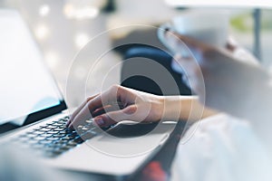 Closeup female freelancer sitting front open laptop computer with blank screen blue monitor with cup of coffee in her hand