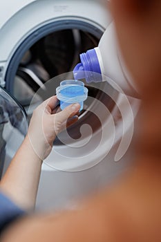 Closeup of female hand detergent or washing liquid in the container with washing machine in background. Hand holding