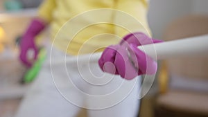 Closeup female hand in glove imitating guitar playing on broom with blurred unrecognizable woman dancing at background