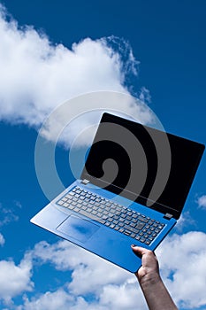 Closeup of female hand holding a blue laptop against the blue sky with white clouds