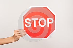 Closeup of female hand holding octagonal Stop symbol, ban concept, arm showing red traffic sign warning of forbidden way