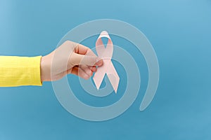 Closeup of female hand holding small pink ribbon, symbol of breast cancer awareness, oncological disease prevention and female