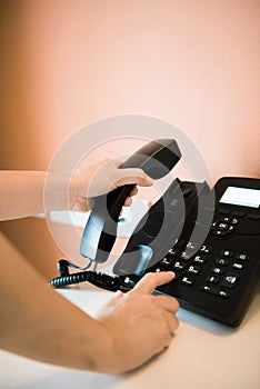 Closeup of female hand holding telephone receiver while dialing a telephone number to make a call using a black landline phone.
