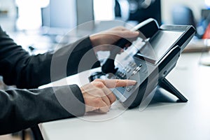 Closeup female hand on landline phone in office. Faceless woman in a suit works as a receptionist answering the phone to
