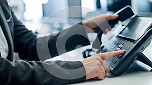 Closeup female hand on landline phone in office. Faceless woman in a suit works as a receptionist answering the phone to