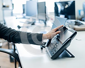 Closeup female hand on landline phone in office. Faceless woman in a suit works as a receptionist answering the phone to