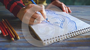 Closeup of female hand painting sketch on paper notebook with pencils. Woman artist at work