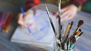 Closeup of female hand painting sketch on paper notebook with pencils. Woman artist at work