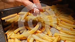 Closeup of female hand pouring salt on frying french fries potatoes on baking pan. Fast food, healthy nutrition, cooking in oven