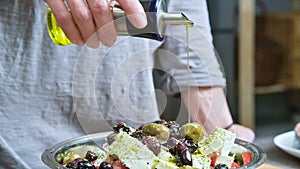 Closeup of a female hand watering fresh vegan greek salad olive oil. Natural food healthy lifestyle