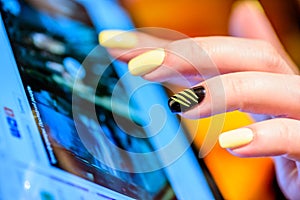 Closeup female hands fingers with yellow nails over tablet screen