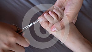 Closeup of female hands holding scissors to cut toe nails on tiny baby foot. Mom taking care of her child s hygiene