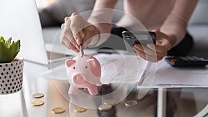 Closeup female hands holding smartphone put euro coin into piggybank