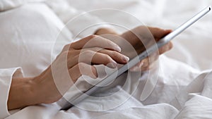 Closeup female hands holding tablet surfing internet lying in bed