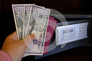 closeup female hands holds American dollars banknotes, personal documents, tourist puts money in hotel mini safe with electronic